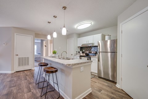 a kitchen with a large island with stools and a stainless steel refrigerator